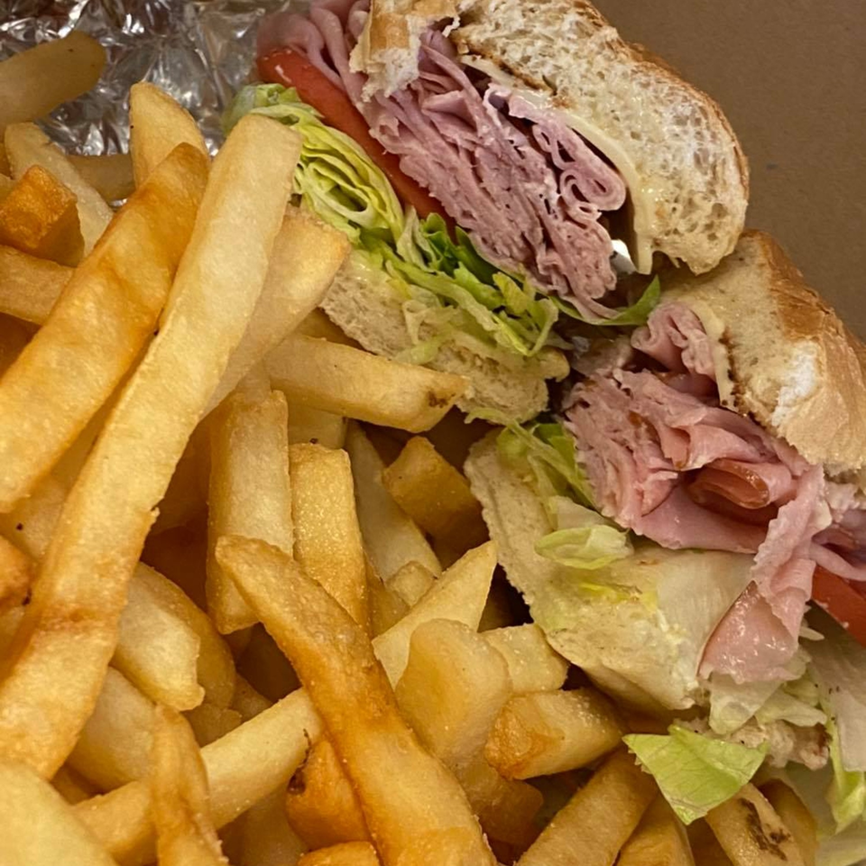 A Bozzy's Pizzeria ham and cheese sub with lettuce and tomato, served with golden french fries.