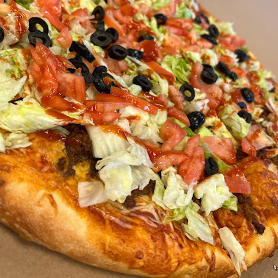 Close-up of a Bozzy's Pizzeria taco pizza with lettuce, tomatoes, black olives, and sauce.