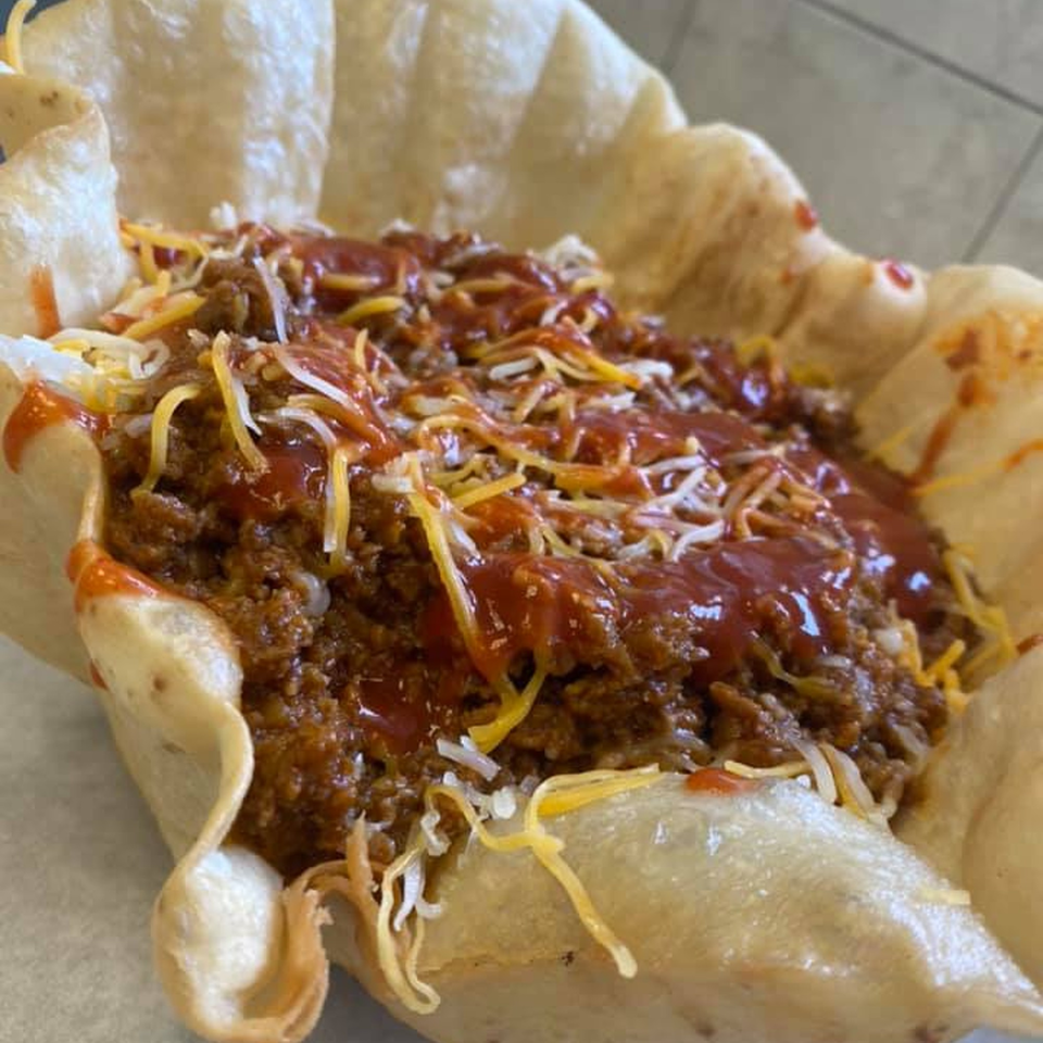 A taco salad in a crispy tortilla bowl, topped with ground meat, cheese, and red sauce.