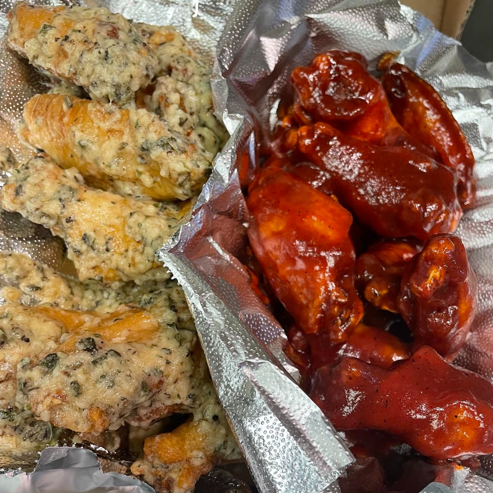 Two types of Bozzy's Pizzeria chicken wings, one creamy garlic parmesan and one spicy red, in foil.